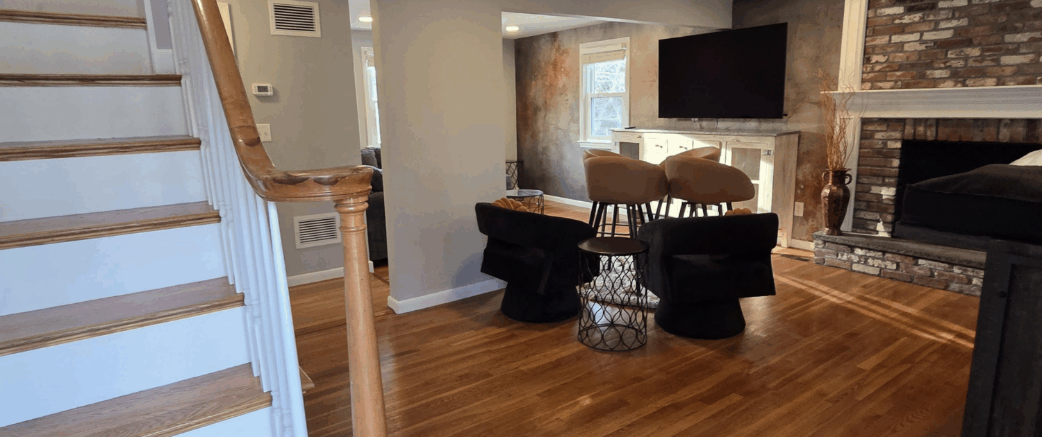 image 1 - J.E.P. Contracting | J.E.P. Contracting Living room interior: staircase with wooden handrail on the left, hardwood floors, gray walls, and a brick fireplace with a mounted TV above a white mantle. | J.E.P. Contracting