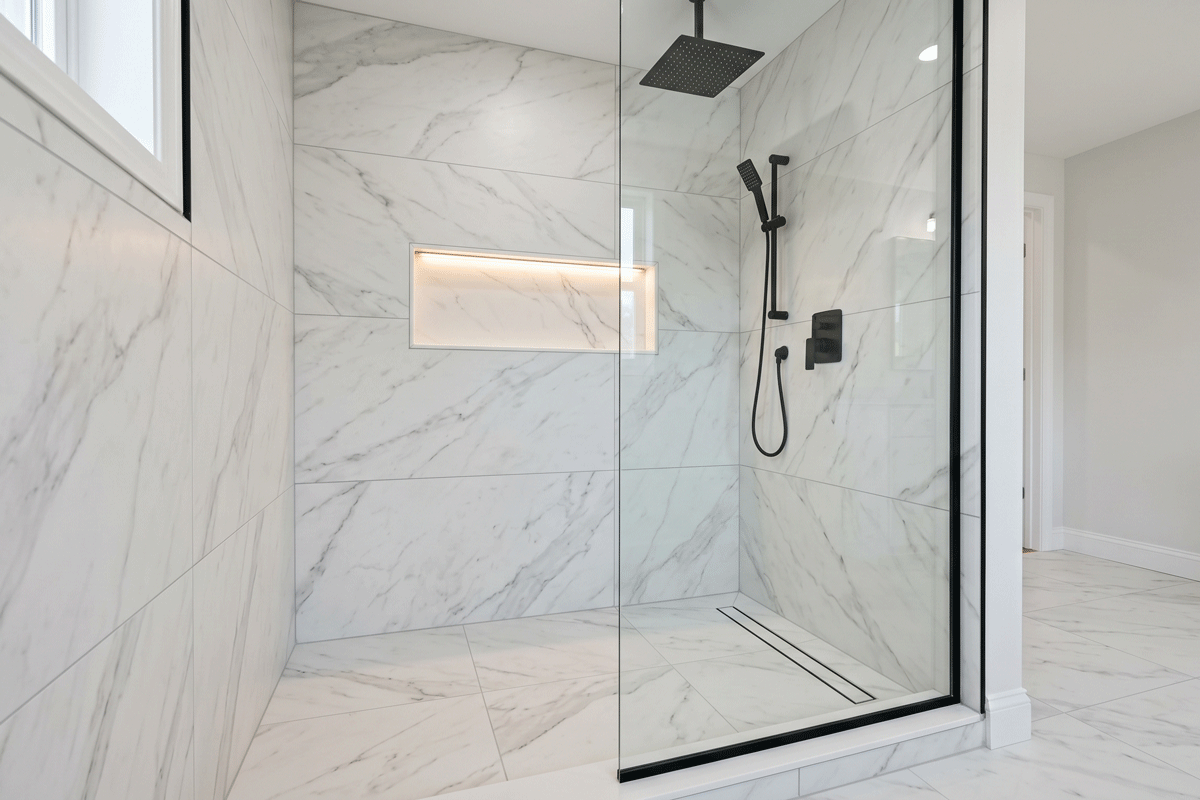 3b1 - J.E.P. Contracting | J.E.P. Contracting Glass-walled shower with white-gray marble tiles and a black rainfall showerhead, handheld wand, and built-in illuminated niche reflection in the glass door | J.E.P. Contracting