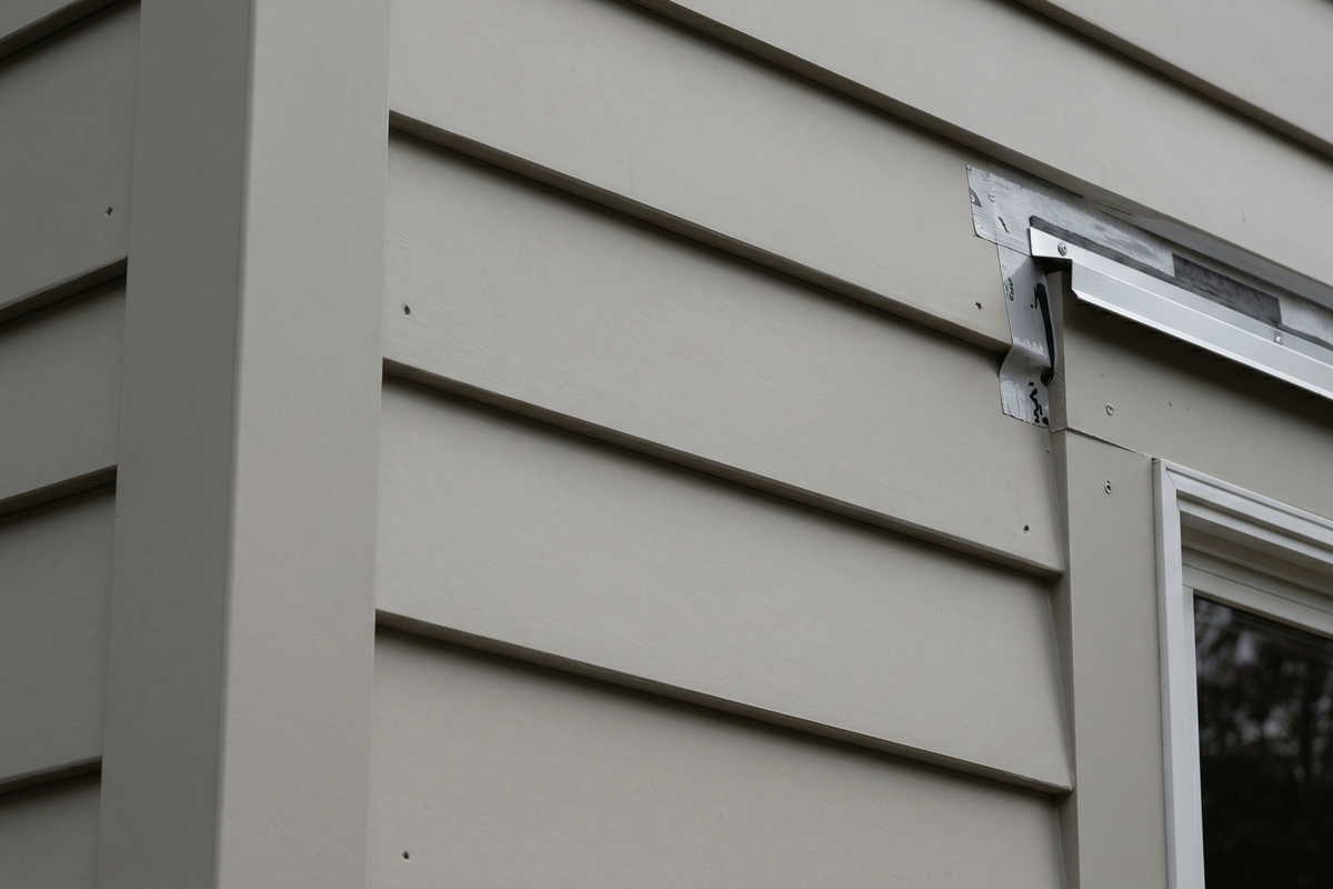 4b1 - J.E.P. Contracting | J.E.P. Contracting Close-up of beige horizontal house siding with a metal flashing/bracket attached near a window on the right. | J.E.P. Contracting