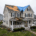 Two-story beige house with a torn roof covered by a blue tarp, a worker on a ladder, and debris scattered across the yard after a storm fall. | J.E.P. Contracting