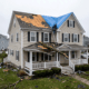 5f - J.E.P. Contracting | J.E.P. Contracting Two-story beige house with a torn roof covered by a blue tarp, a worker on a ladder, and debris scattered across the yard after a storm fall. | J.E.P. Contracting